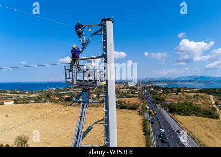 Chalkidiki, Griechenland - Juli 12, 2019: Elektriker sind Klettern auf elektrischen Polen Stromleitungen zu installieren und reparieren Nach dem heftigen Sturm, t Struck Stockfoto