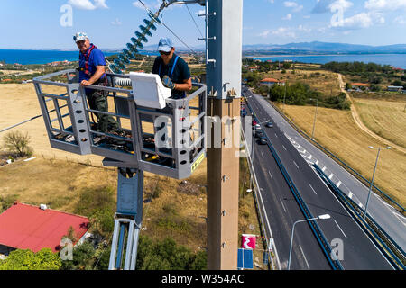 Chalkidiki, Griechenland - Juli 12, 2019: Elektriker sind Klettern auf elektrischen Polen Stromleitungen zu installieren und reparieren Nach dem heftigen Sturm, t Struck Stockfoto