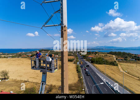 Chalkidiki, Griechenland - Juli 12, 2019: Elektriker sind Klettern auf elektrischen Polen Stromleitungen zu installieren und reparieren Nach dem heftigen Sturm, t Struck Stockfoto