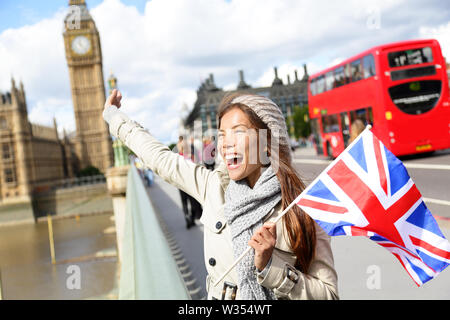 London - Ihnen gerne touristische Holding britische britische Flagge von Big Ben und roten Doppeldeckerbusses. Aufgeregt Mädchen sightseeing Reisen auf die Westminster Bridge, London, England, Vereinigtes Königreich. Multirassischen asiatischen Kaukasischen Stockfoto