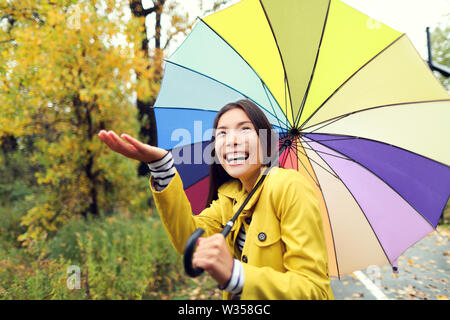 Herbst/Herbst Konzept - Frau unter Regen mit Regenschirm aufgeregt. Schöne junge Frauen tragen Regenjacke im Regen überrascht und begeistert. Gemischte Rasse asiatischen Kaukasische Mädchen in ihrem 20s zu Fuß in den Wald. Stockfoto