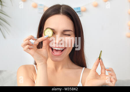 Junge Frau Rest zu Hause Beauty Care sitzen Holding Gurkenscheiben lächelnd verspielten close-up Stockfoto