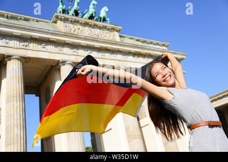 Deutsche Fahne - eine Frau in Berlin Brandenburger Tor glücklich jubelnd Feiern wehende Flagge von Brandenburger Tor, Deutschland. Fröhlich aufgeregt multirassischen Frau in Deutschland Travel Concept. Stockfoto