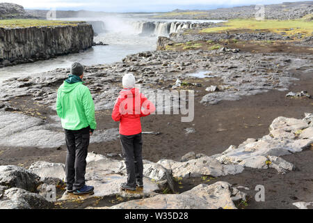 Island Natur Landschaft mit Menschen, die von Selfoss Wasserfall. Wanderer genießen Blick auf den berühmten isländischen touristische Attraktion Ziel. Wandern Paar unter Bruch von Selfoss in Vatnajökull National Park. Stockfoto