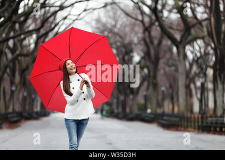 Frau mit roten Regenschirm spazieren im Park im Herbst. Glücklich lächelnde gemischtrassigen Mädchen gehen fröhlich mit roten Regenschirm im Central Park, Manhattan, New York City, USA. Stockfoto