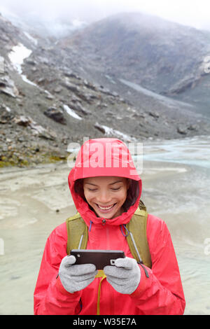 Smart phone Frau sms sms-App auf dem Smartphone mit Touchscreen Handschuhe. Happy Wanderer mit Handy in der freien Natur in Rain. Mädchen mit Handschuh von leitfähigen Gewebe für Touch Screen. Stockfoto