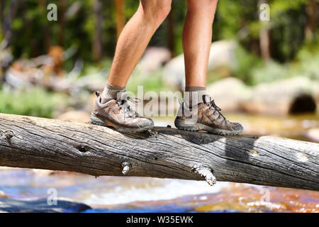 Wandern mann Fluß zu Fuß in das Gleichgewicht gefallenen Baumstamm in der Natur Landschaft. Nahaufnahme der männlichen Wanderer Trekking Schuhe draussen im Wald auf Baum. Balance challenge Konzept. Stockfoto