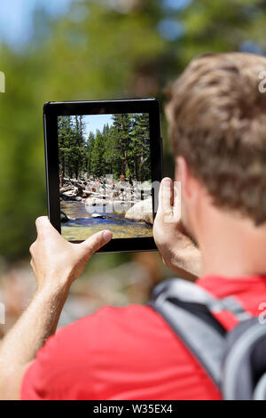 Wandern Wanderer Mann die Bilder von Wald auf digital Tablet Computer. Junge Erwachsene tun mobile Fotografie der Natur Landschaft im Yosemite National Park, Kalifornien, USA. Stockfoto