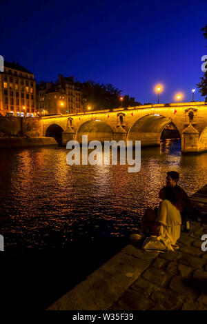 Junges Paar an der Brücke Pont Marie, beleuchtet bei Nacht Ile Saint Louis, an der seine, Paris, Frankreich. Stockfoto