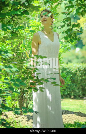 Junge schöne Mädchen in einem weißen Kleid close-up auf dem Hintergrund des grünen Büschen mit blühenden Jasmin. Stockfoto