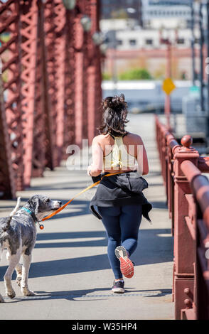 Das Mädchen in Sportkleidung macht ein Run auf die Brücke, um Gewicht zu verlieren und ihr Körper in einer attraktiven Form halten, und auch Ihr Hund an der Leine, die ru zu Fuß Stockfoto