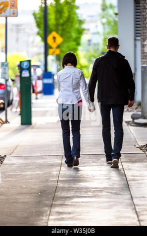 Schlanke curly Frau und hohen schlanken Mann gehen, Hände auf den Bürgersteig auf einer Straße der Stadt, die Ihre warmen Gefühle zueinander, wodurch Sy Stockfoto