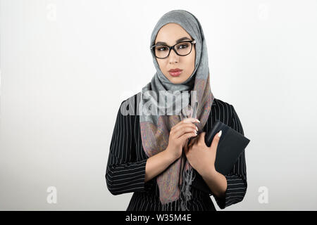Junge schöne muslimische Frau mit Brille turban Hijab, Kopftuch, ein Notizbuch und einen Stift isoliert weißer Hintergrund Stockfoto