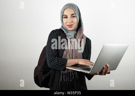 Junge attraktive Muslimische Schüler mit Rucksack Holding, und tippen Sie auf Ihrem Laptop das Tragen von Turban hijab Kopftuch weißem Hintergrund Stockfoto