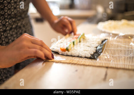 Eine Frau vorbereiten Hausgemachte Sushi und Brötchen. Die Sushi. Der Prozess der Vorbereitung Rolling Sushi. Stockfoto