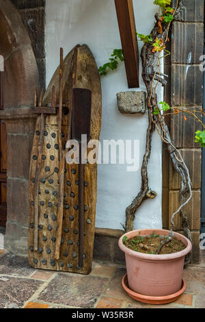 Alte vintage traditionelle Dreschmaschine aus Holz und Flint Stone mit anderen landwirtschaftlichen Geräten an die Wand und eine alte große und lange Weinstock lehnte Stockfoto