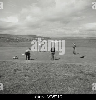 1950er Jahre, historisch, vier männliche Amateur-Golfspieler auf einem Putting Green auf dem Portstewart Golf Course, einem Links Golf Course in Co. Antrim, Nordirland, an der altantischen Mündung des Lough Foyle. Das Golfspiel auf dem Gelände von Portstewart geht auf das Jahr 1889 zurück und der Golfclub wurde 1894 gegründet. Stockfoto