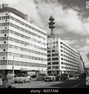 1960er Jahre, historische Stadtszene mit großen Gebäuden, darunter das Hotel Kokusai Kanko, Büros, einem Telekommunikationsturm und Autos der Epoche, Marunouchi, Tokio, Japan. Das Hotel befindet sich in der Altstadt, in der Nähe des Bahnhofs Shimbashi, das Kokusai Kanko Hotel - buchstäblich "International Tourist Hotel" - war ein großes Hotel mit 626 Zimmern und war Teil des Bauboom, der in der Stadt vor und nach den Olympischen Sommerspielen 1964 stattfand. Stockfoto