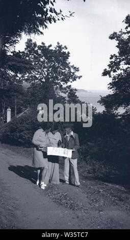 1930er Jahre, historischer Herr und zwei Damen im Urlaub auf einem Pfad über der Küste mit Blick auf eine Karte, England, Großbritannien. Stockfoto