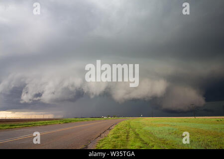 Ein großer Superzelle Gewitter mit Shelf cloud und ein wall cloud Webstühle über eine Straße in der ländlichen Landschaft. Stockfoto