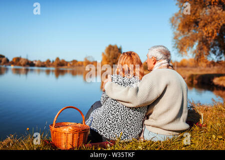 Senior paar Picknick im Herbst See. Glücklich der Mann und die Frau die Natur genießen und umarmen. Romantisches date Stockfoto