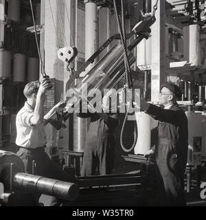 1950er Jahre, historische männliche Arbeiter in den Druckwerken von Hazell, Watson & Viney, die eine Riemenscheibe halten, während sie eine Edelstahltrommel bewegen, England, Großbritannien. Mit Sitz in Aylesbury, Buckinghamshire, war das Druck- und Verlagsunternehmen, das 1839 seine Geschäftstätigkeit aufnahm und nach dem 2. Weltkrieg stark wuchs. In den frühen 1960er Jahren fusionierte sie mit Purnell & Sons zur British Printing Corporation (BPC), eine Firma, die 1981 von Pressebaron Robert Maxwell übernommen wurde. Stockfoto