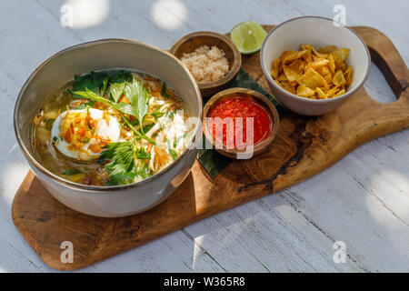 Soto Ayam, einem gelben scharfe Hühnersuppe mit gekochtem Ei, Petersilie und Bawang Goreng (gebratene Schalotten). Mit Kalk serviert, würzige sambal Sauce, Kartoffelchips Stockfoto