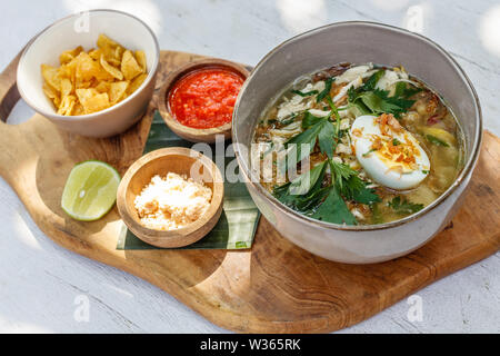 Soto Ayam, einem gelben scharfe Hühnersuppe mit gekochtem Ei, Petersilie und Bawang Goreng (gebratene Schalotten). Mit Kalk serviert, würzige sambal Sauce, Kartoffelchips Stockfoto