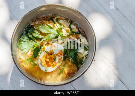 Soto Ayam, einem gelben scharfe Hühnersuppe serviert mit gekochtem Ei, Petersilie und Bawang Goreng (gebratene Zwiebel). Traditionelle indonesische Küche. Stockfoto