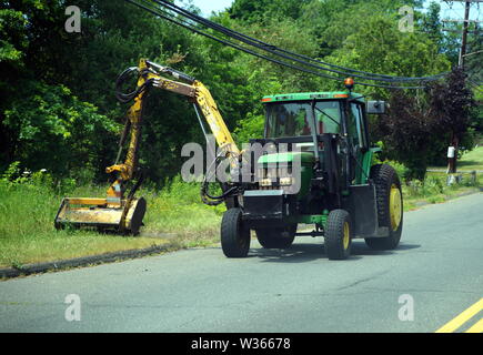 Traktor mit einer hydraulischen Mäher attachment mähen Straßenrand Gras von der Straße. Stockfoto