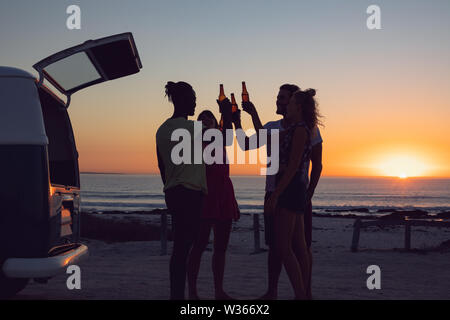 Freunde toasten Bierflaschen in der Nähe von Wohnmobil bei Sonnenuntergang Stockfoto