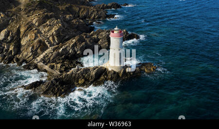 Ansicht von oben, beeindruckende Luftaufnahme eines alten und schönen Leuchtturm auf einer felsigen Küste durch eine raue Meer umspült. Faro di Capo Ferro. Stockfoto