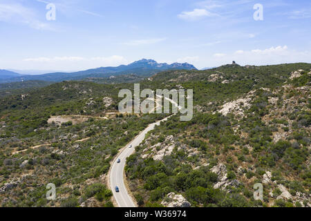 Ansicht von oben, atemberaubenden Blick auf einige Autos, die entlang einer Straße durch einen grünen Wald flankiert wird. Sardinien, Italien. Stockfoto