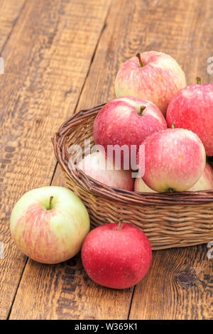 Rote Äpfel mit Wassertropfen im Weidenkorb und auf alten Brettern. Ansicht von oben Stockfoto