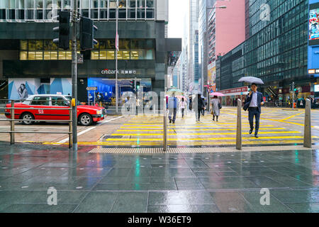 Central, Hong Kong - 14. März 2019: Menschen zu Fuß und über die Straße an einem regnerischen Tag. Stockfoto
