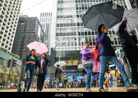 Central, Hong Kong - 14. März 2019: Massen von Menschen zu Fuß und über die Straße an einem regnerischen Tag. Stockfoto