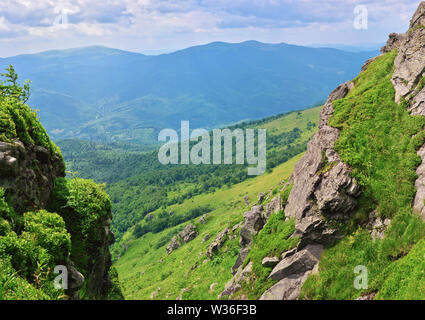 Felsen auf Pikuy Berg gegen das Tal unter majestätischen Green mountain Hills in Wiesen und Wald bedeckt. Bewölkt Sommer Tag im Sommer. Ukraine, Lv Stockfoto