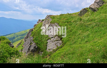 Felsen auf Pikuy Berg gegen das Tal unter majestätischen Green mountain Hills in Wiesen und Wald bedeckt. Bewölkt Sommer Tag im Sommer. Ukraine, Lv Stockfoto