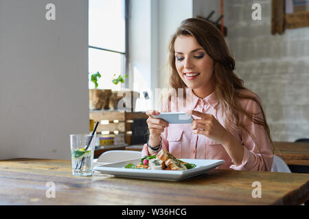 Junge Frau, die ihre Mahlzeit im Restaurant fotografieren Stockfoto