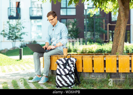 Mann, der Smart watch Arbeiten am Laptop sitzen in der Nähe von Tree Stockfoto