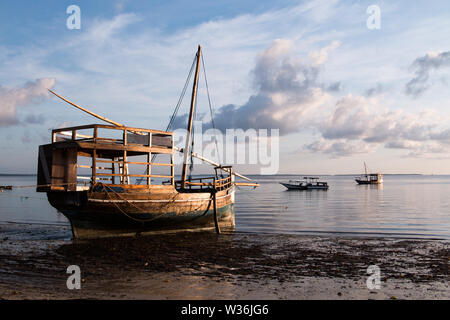 Ein großes hölzernes Segel Boot auf dem Wasser am Strand bei Sonnenaufgang in Mafia Island, Tanzania, mit bewölktem Himmel und ruhiges Wasser. Stockfoto