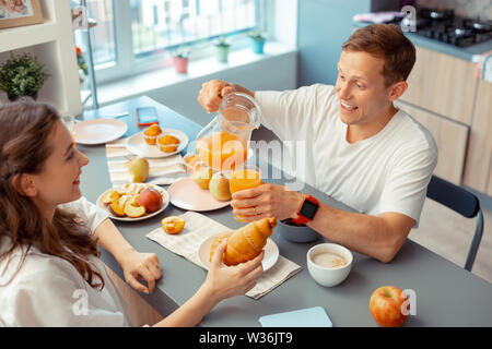 Pflege Mann gießen einige Saft für seine Frau essen Croissant Stockfoto
