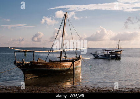 Ein großes hölzernes Segel Boot auf dem Wasser am Strand bei Sonnenaufgang in Mafia Island, Tanzania, mit bewölktem Himmel und ruhiges Wasser. Stockfoto