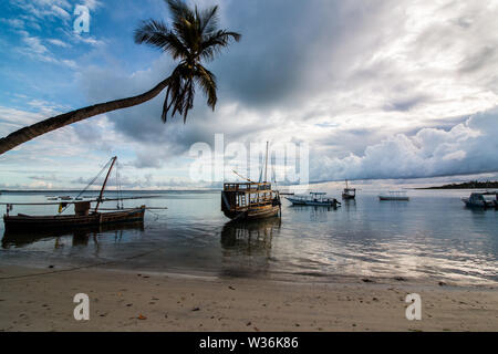 Kleine Segelboote auf dem Wasser am Strand bei Sonnenaufgang in Mafia Island, Tanzania, mit bewölktem Himmel und ruhiges Wasser mit umliegenden dugout Kanus. Stockfoto