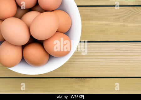 Nahaufnahme von Eiern in einer weißen Schüssel auf einem rustikalen Holztisch - direkt über. Das gesunde Essen/Frühstück Konzept. Stockfoto