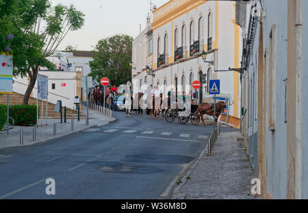 Ein Pferd angetrieben schwarz Beförderung seinen Weg durch die engen Straßen von Estoi zusammen mit Reiter aller Altersklassen und Geschlechter an einem Abend wenden. Portugal. Stockfoto