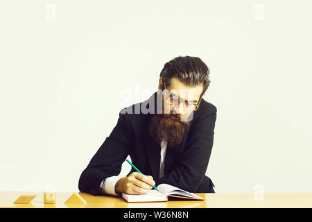 Die Jungen gut aussehenden bärtigen Mann Wissenschaftler oder Professor mit langem Bart und Lehrer Gläser mit Buch oder Briefpapier am Tisch sitzen mit Holzwürfeln isolat Stockfoto