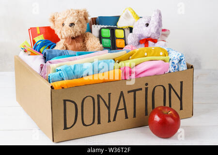 Verschiedene Spenden in einer Box - Kleidung, Schreibwaren und Spielwaren. Kleidung für Kinder und Jugendliche. Vorbereitung für die Schule. Stockfoto
