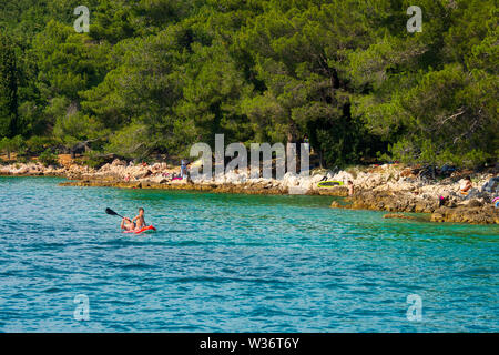 Vater und Sohn paddeln entlang der kroatischen Küste in der Nähe von Malinska auf der Insel Krk, Kroatien, mit reichlich Sonnenanbeter im Hintergrund Stockfoto