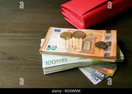 Euro-banknoten und -Münzen mit verschiedenen Kreditkarten und eine rote Mappe im Hintergrund Stockfoto